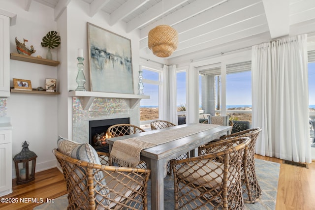 dining room with a tile fireplace, beam ceiling, visible vents, and wood finished floors