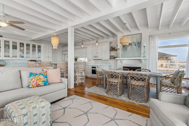 living room with a lit fireplace, wood finished floors, beam ceiling, and a ceiling fan