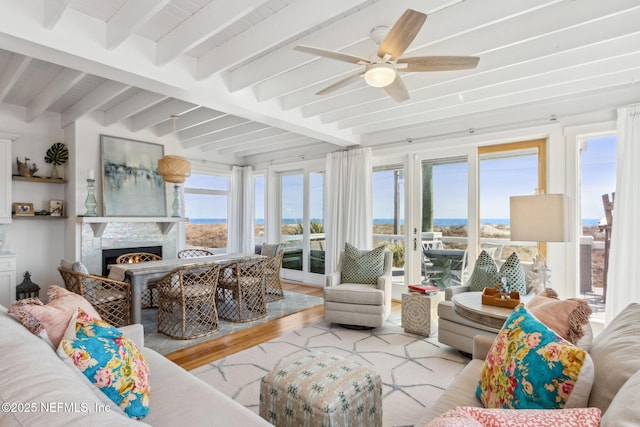 sunroom / solarium with a warm lit fireplace, ceiling fan, and beam ceiling