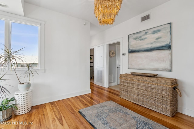 hall featuring baseboards, visible vents, an inviting chandelier, and wood finished floors