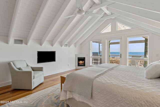 bedroom featuring a warm lit fireplace, vaulted ceiling with beams, baseboards, and wood finished floors