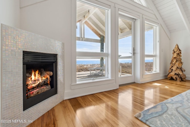 interior space with vaulted ceiling with beams, a tiled fireplace, and wood finished floors