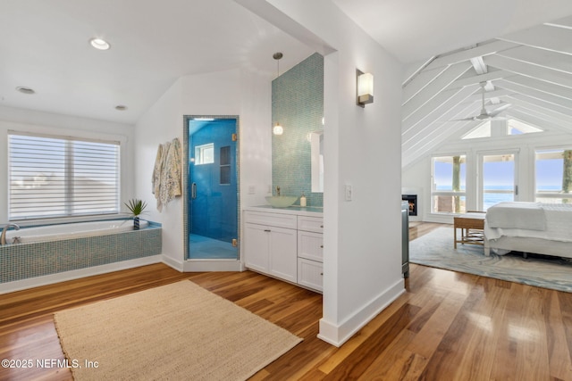 bathroom with ensuite bathroom, a warm lit fireplace, wood finished floors, vanity, and a stall shower