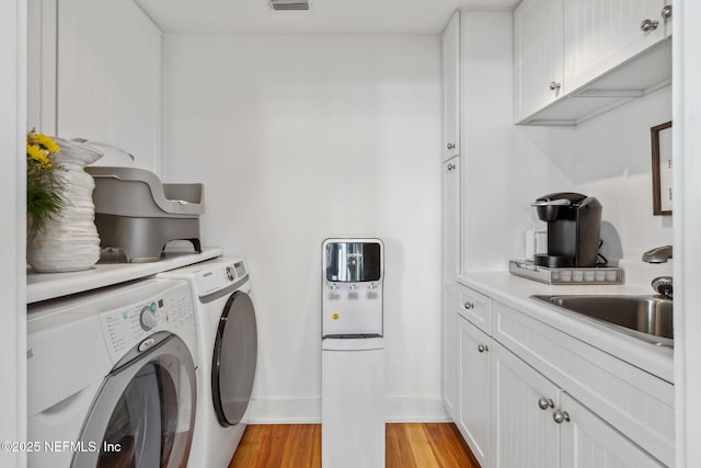 laundry area featuring cabinet space, visible vents, washer and dryer, light wood-style floors, and a sink