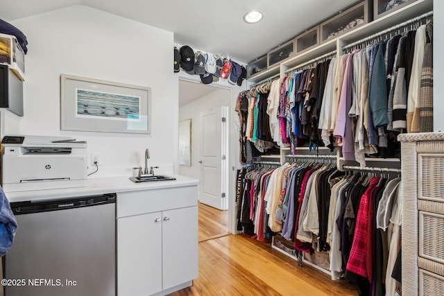 walk in closet with light wood-style flooring, vaulted ceiling, and a sink