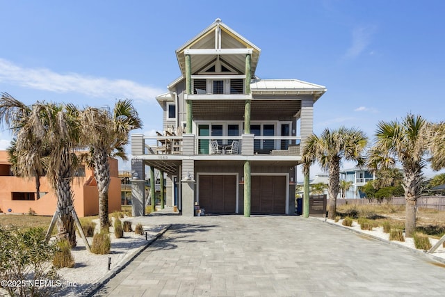 coastal home with metal roof, a balcony, a garage, decorative driveway, and a standing seam roof