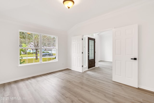 unfurnished room with lofted ceiling, light wood-type flooring, baseboards, and crown molding