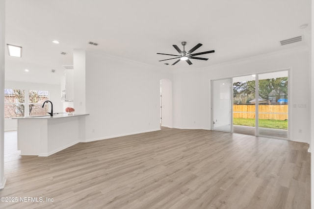 unfurnished living room featuring arched walkways, crown molding, visible vents, light wood-style flooring, and plenty of natural light