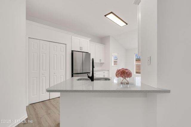 kitchen featuring a peninsula, white cabinets, a sink, and freestanding refrigerator