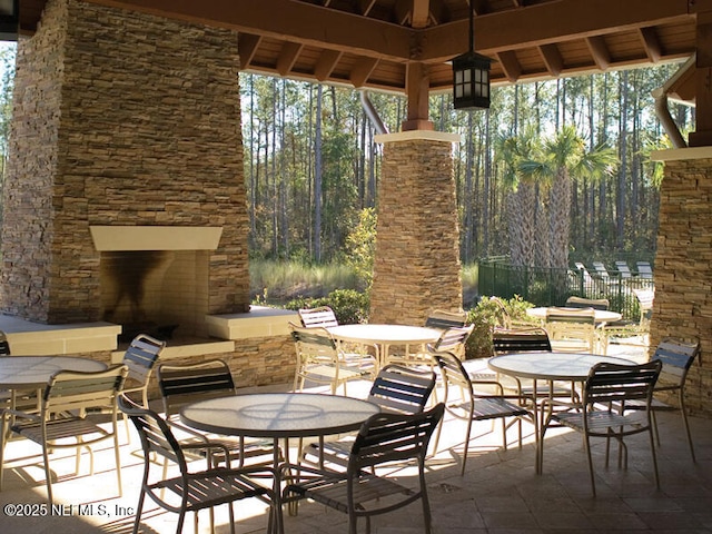 view of patio featuring an outdoor stone fireplace, fence, outdoor dining area, and a gazebo