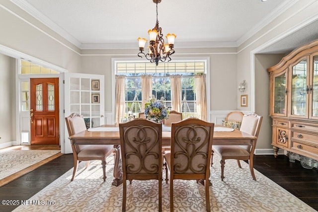 dining space with dark wood-style flooring, a notable chandelier, crown molding, and a wainscoted wall