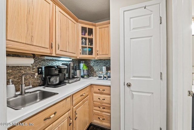 kitchen featuring tasteful backsplash, light countertops, light brown cabinetry, glass insert cabinets, and a sink