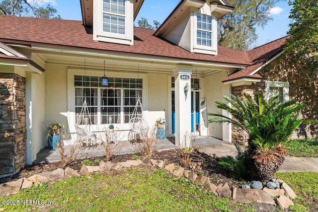 view of front of home featuring stone siding, a shingled roof, a porch, and stucco siding