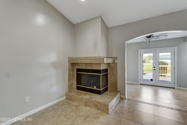 unfurnished living room with french doors, a fireplace, a ceiling fan, tile patterned flooring, and baseboards