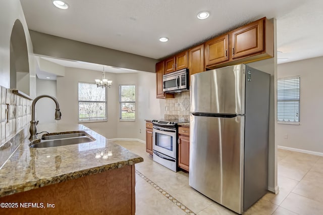 kitchen with light stone counters, brown cabinets, stainless steel appliances, a sink, and recessed lighting