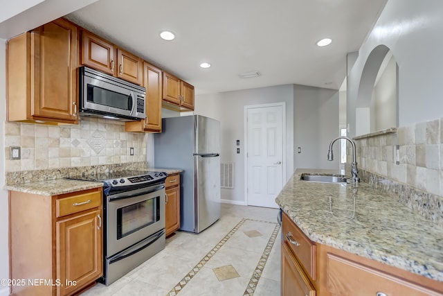 kitchen with light stone counters, stainless steel appliances, recessed lighting, visible vents, and a sink