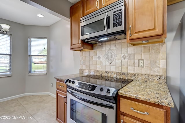 kitchen with baseboards, decorative backsplash, brown cabinets, light stone countertops, and stainless steel appliances