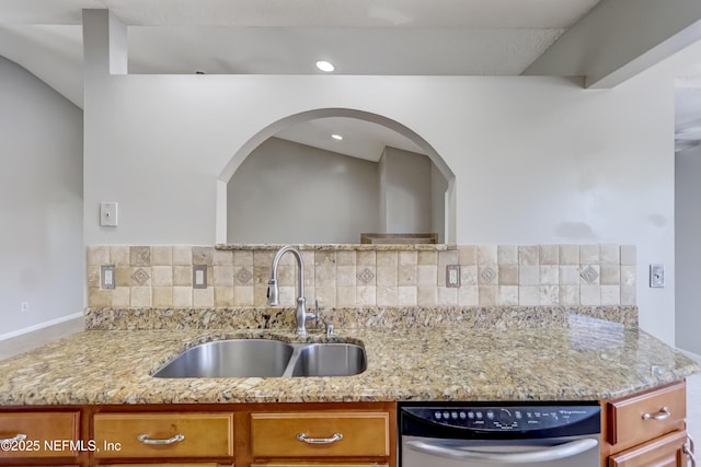 kitchen featuring decorative backsplash, dishwasher, brown cabinetry, light stone counters, and a sink