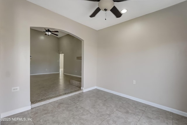 tiled spare room with arched walkways, ceiling fan, and baseboards