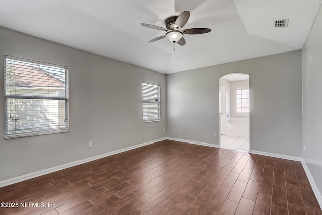 spare room featuring arched walkways, ceiling fan, visible vents, baseboards, and dark wood-style floors