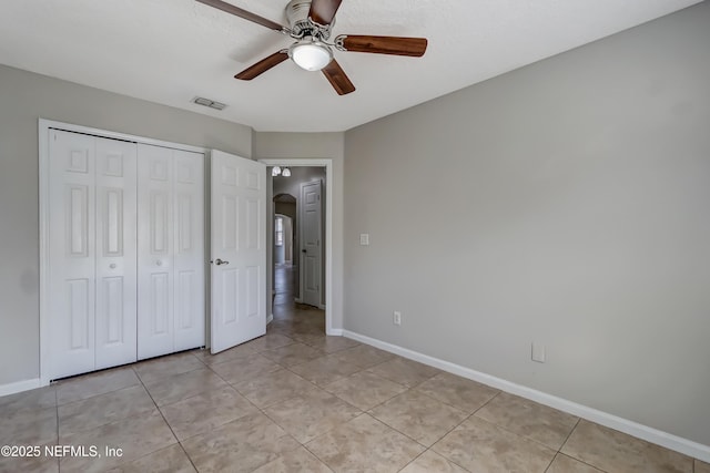 unfurnished bedroom with arched walkways, light tile patterned floors, visible vents, baseboards, and a closet