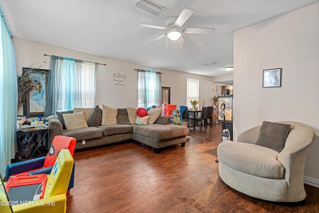 living room featuring a textured ceiling, dark wood-style flooring, visible vents, and a ceiling fan