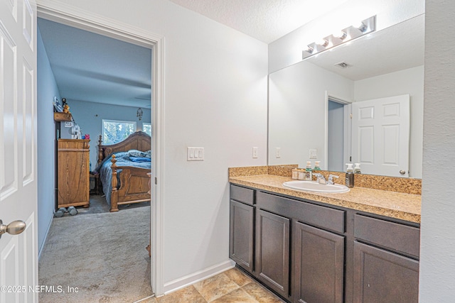 ensuite bathroom with a textured ceiling, connected bathroom, visible vents, vanity, and baseboards