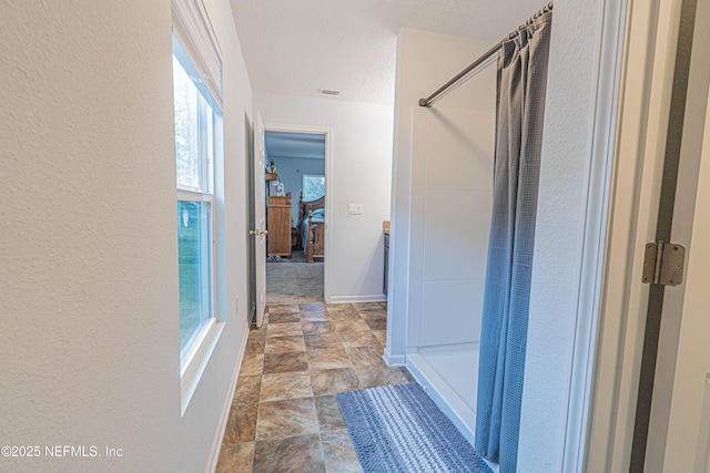 ensuite bathroom featuring a textured ceiling, ensuite bathroom, curtained shower, baseboards, and stone finish flooring