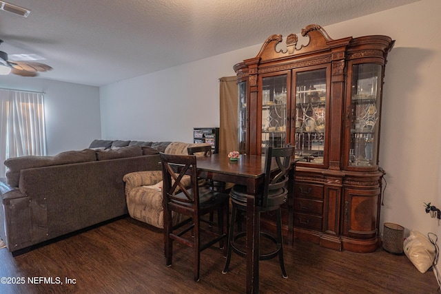 dining area featuring a textured ceiling, dark wood finished floors, visible vents, and a ceiling fan