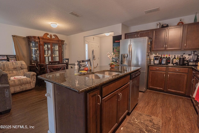 kitchen with a textured ceiling, stainless steel appliances, dark wood-type flooring, a sink, and dark stone counters