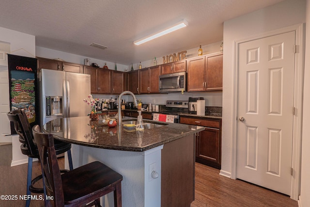 kitchen with a textured ceiling, stainless steel appliances, a breakfast bar, a sink, and dark wood finished floors