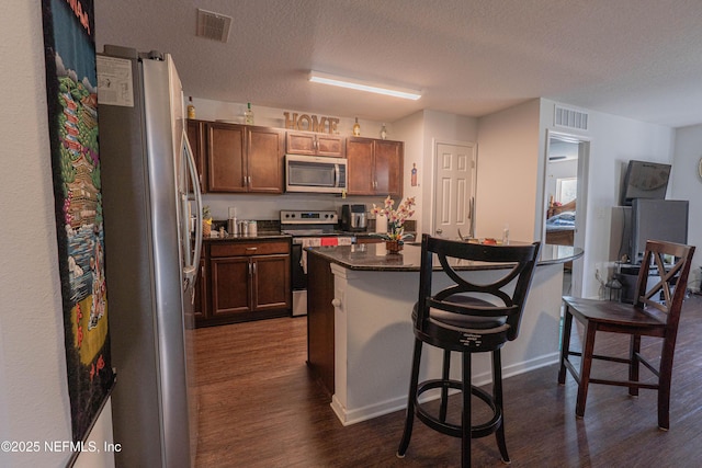 kitchen featuring a breakfast bar, visible vents, appliances with stainless steel finishes, dark countertops, and dark wood finished floors