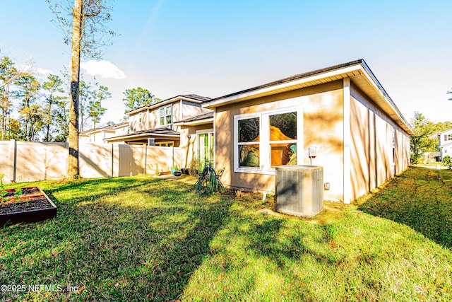 back of property with central air condition unit, stucco siding, fence, and a yard