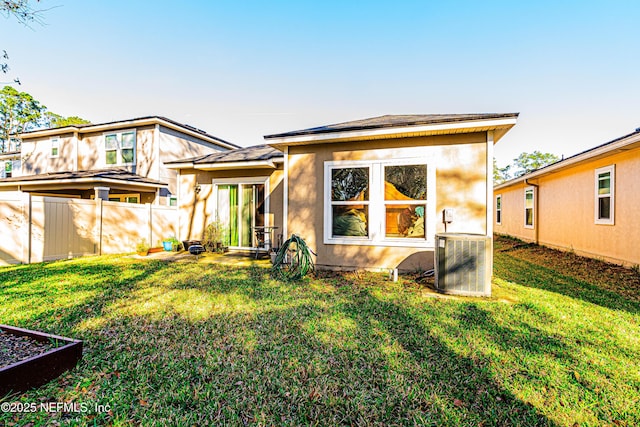 rear view of property with a yard, stucco siding, fence, and central air condition unit