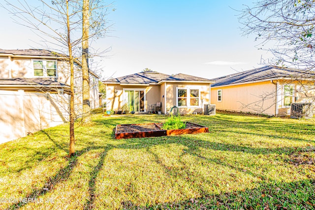 back of house with stucco siding, a lawn, fence, cooling unit, and a garden