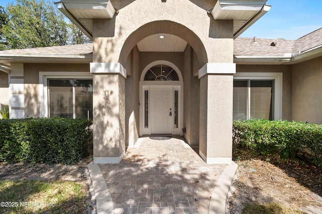 view of exterior entry with roof with shingles and stucco siding