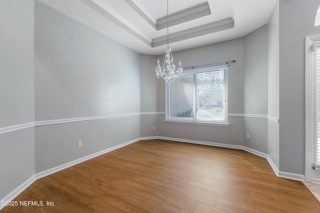 empty room with a raised ceiling, a textured ceiling, wood finished floors, a chandelier, and baseboards