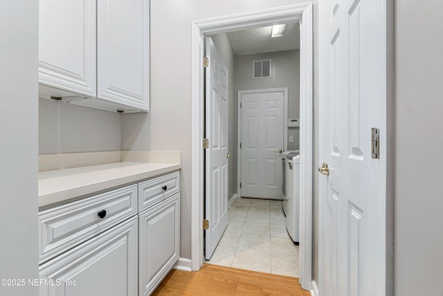 laundry room with light tile patterned floors, a textured ceiling, washing machine and dryer, and visible vents