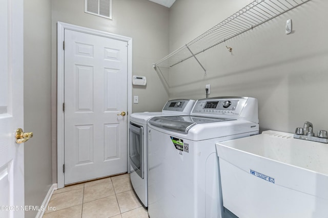 clothes washing area with light tile patterned flooring, laundry area, a sink, visible vents, and washer and dryer