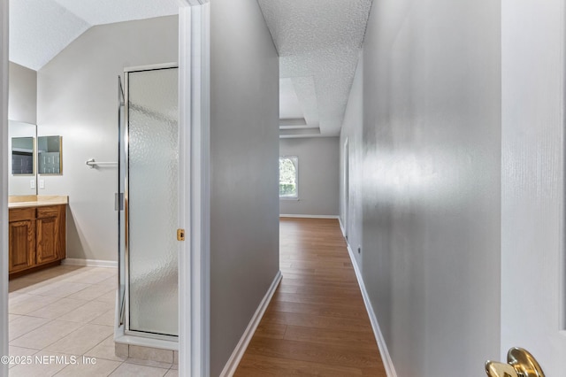 hallway featuring light wood-style floors, a textured ceiling, and baseboards
