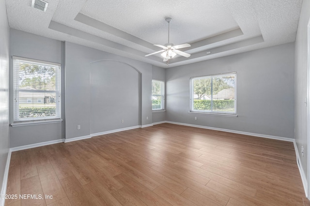 unfurnished room with a tray ceiling, visible vents, baseboards, and wood finished floors