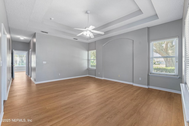 empty room with light wood-type flooring, plenty of natural light, baseboards, and a tray ceiling