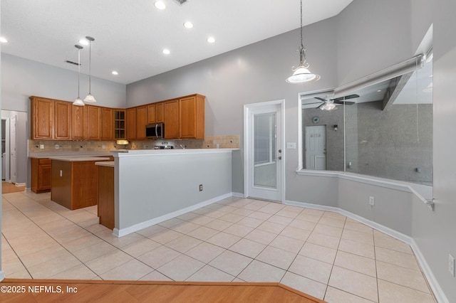 kitchen featuring brown cabinets, stainless steel microwave, a ceiling fan, light tile patterned flooring, and high vaulted ceiling
