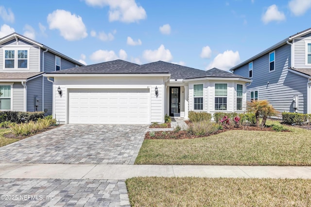 view of front facade with a garage, roof with shingles, decorative driveway, and a front yard