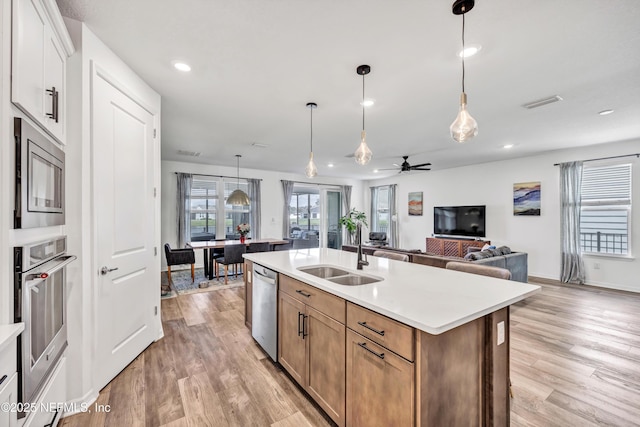 kitchen with white cabinets, appliances with stainless steel finishes, open floor plan, a kitchen island with sink, and light countertops