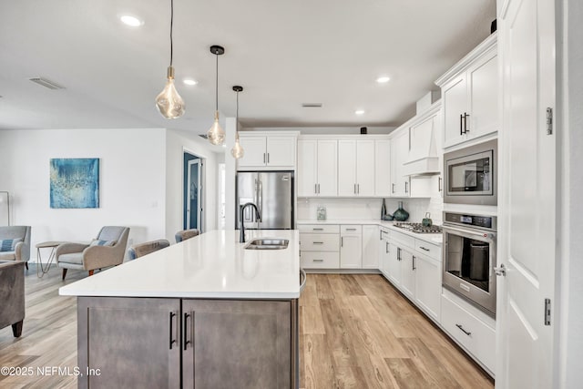 kitchen with stainless steel appliances, an island with sink, light countertops, and white cabinets