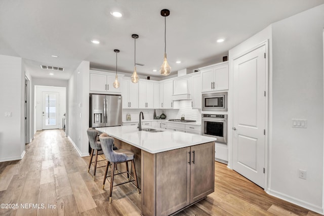 kitchen with stainless steel appliances, light countertops, white cabinets, a sink, and an island with sink