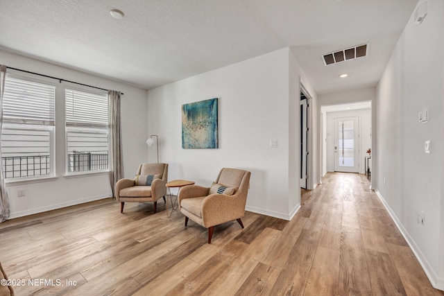 living area with light wood finished floors, baseboards, visible vents, and a textured ceiling