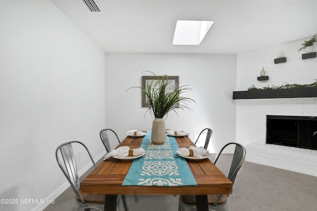 dining space with a skylight, visible vents, a brick fireplace, carpet flooring, and baseboards