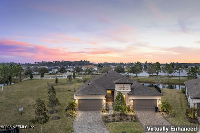 view of front of house featuring decorative driveway, a water view, an attached garage, fence, and stone siding